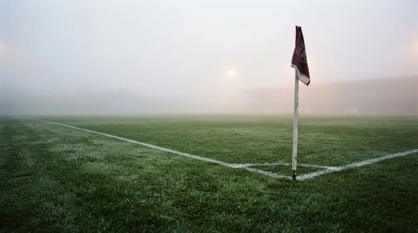 Der Rand eines Spielfelds mit weißer Linie und Eckfahne bei Nebel am frühen Morgen, ohne Menschen.
