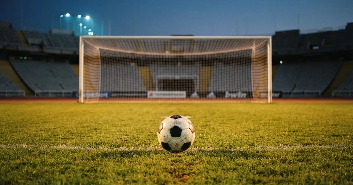Ein Fußball liegt im Strafraum direkt vor dem Tor mit Netz, im Hintergrund leere Ränge bei Dämmerung.
