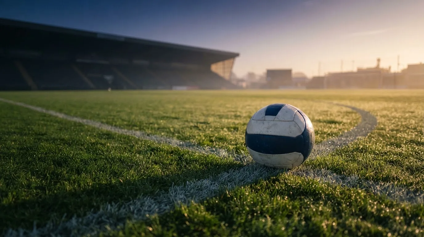 Ein Fußball liegt am Rand des Mittelkreises auf einem leeren Rasenplatz bei Sonnenaufgang.