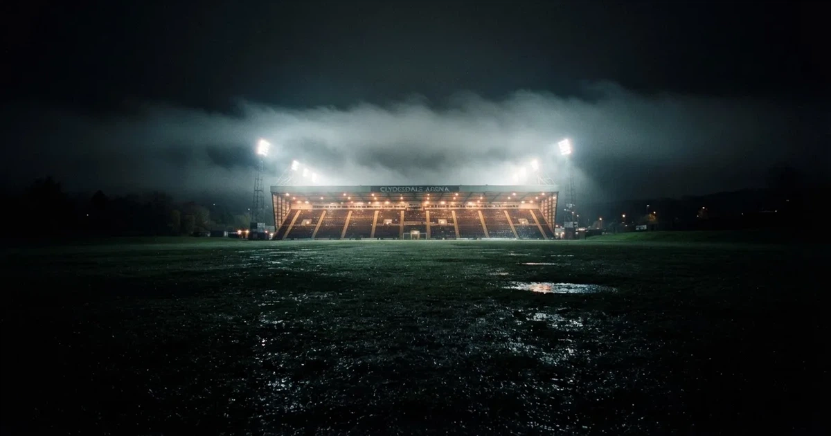 Ein Stadion unter Flutlicht, aus großer Entfernung über eine dunkle Wiese fotografiert, am Himmel zieht Nebel auf.