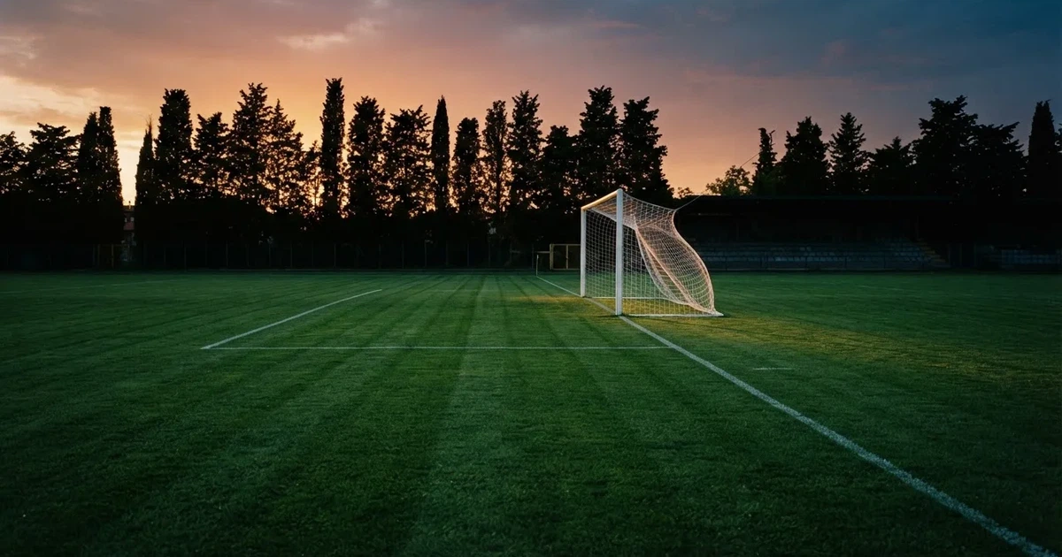 Ein Fußballtor mit Netz auf einem leeren Platz im Abendlicht, der Rasen frisch gemäht, im Hintergrund Zypressen.