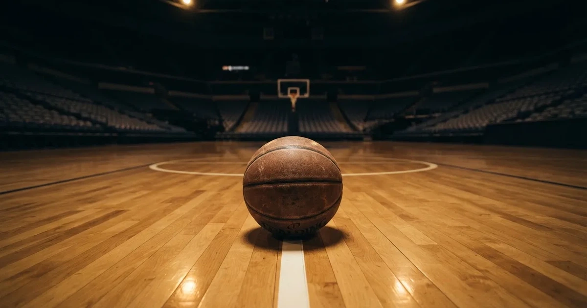 Ein Basketball liegt auf dem Parkettboden einer leeren Arena, Scheinwerfer werfen Licht auf die Mittellinie.